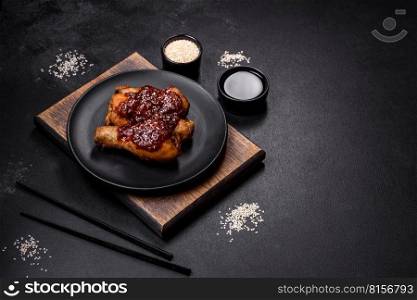 Tasty spicy chicken legs with teriyaki sauce and sesame seeds on a dark concrete background. Tasty spicy chicken legs with teriyaki sauce and sesame seeds