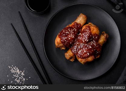 Tasty spicy chicken legs with teriyaki sauce and sesame seeds on a dark concrete background. Tasty spicy chicken legs with teriyaki sauce and sesame seeds