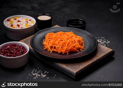 Tasty spicy Korean carrot with spices and herbs on a dark concrete background. Tasty spicy Korean carrot with spices and herbs