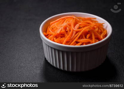 Tasty spicy Korean carrot with spices and herbs on a dark concrete background. Asian food. Tasty spicy Korean carrot with spices and herbs on a dark concrete background