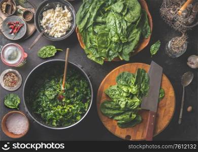 Tasty stewed spinach cooking preparation with cooking pot , ingredients and kitchen utensils. Wooden cutting board with knife. Seasoning and spices. Home cuisine. Top view. Healthy green food