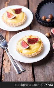 tasty tartlets with custard cream and figs on wooden background