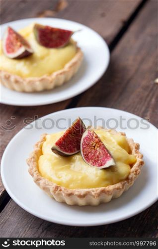 tasty tartlets with custard cream and figs on wooden background