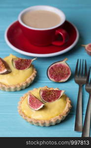 tasty tartlets with custard cream and figs with a cup of coffee on a blue background