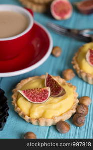 tasty tartlets with custard cream and figs with a cup of coffee on a blue background