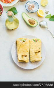 Tasty tortilla wraps sandwiches with avocado and fresh vegetables ingredients on light table background, top view. Healthy food. Vegetarian lunch or snack