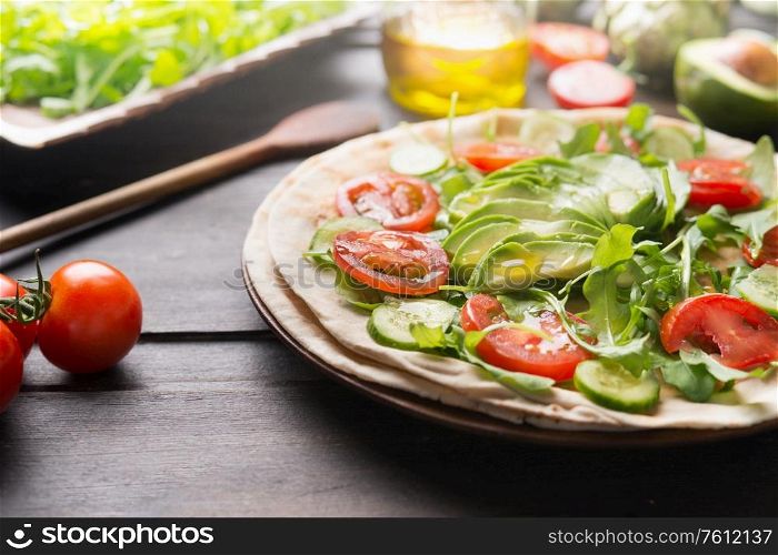 Tasty vegan tortilla wrap preparation. Close up of fresh salad vegetables with sliced avocado and olives oil on rustic table. Healthy clean food concept. Lunch idea. Summer food