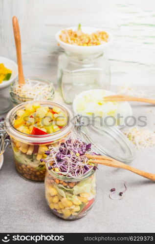 Tasty vegetables salads in jars with corn and sprouts on light rustic kitchen table, close up. Healthy lifestyle or diet food concept