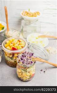 Tasty vegetables salads in jars with corn and sprouts on light rustic kitchen table, close up. Healthy lifestyle or diet food concept