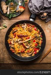 Tasty vegetarian fried noodles pan with vegetables and creamy pasta sauce on wooden background, top view