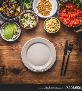 Tasty vegetarian ingredients for healthy meal in bowls: chick peas puree, roasted vegetables , red paprika stew, avocado and seeds served with empty plate with cutlery Clean eating food concept