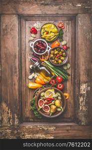 Tasty vegetarian or vegan food cooking ingredient with pickled vegetables, olives , olives oil, green organic almonds lemon and figs on vintage wooden background with kitchen utensils. Top view.