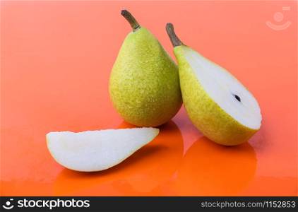 Tasty wet pears on an orange background - A pear cut in half, a piece and a whole pear - Sweet, ripe pears. Tasty wet pears on an orange background - A pear cut in half, a piece and a whole pear
