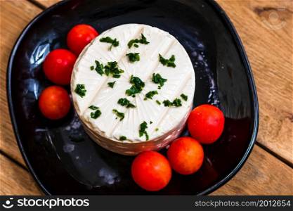 Tasty white cheese with spices and cherry tomatoes on cutting board