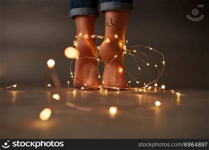 Tattoo feet of the woman decorated with a festive Christmas garland on a dark background. Holiday concept. Feet of the woman decorated with a festive Christmas garland on a dark background.