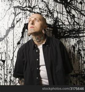 Tattooed and pierced man standing against paint splattered background.