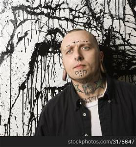 Tattooed and pierced man standing against paint splattered background.