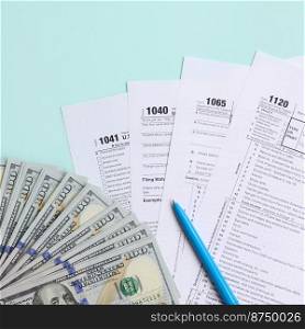 Tax forms lies near hundred dollar bills and blue pen on a light blue background. Income tax return.. Tax forms lies near hundred dollar bills and blue pen on a light blue background. Income tax return