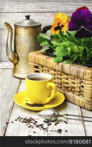 tea and flower pansy. Yellow porcelain cup with tea and basket of decorative Pansy