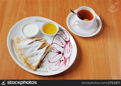 Tea and pancakes with powdered sugar. The dish is decorated by cowberry jam