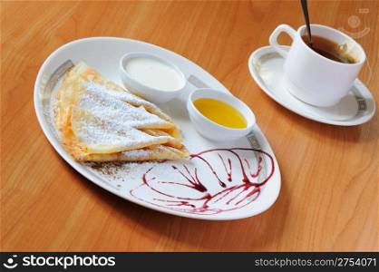 Tea and pancakes with powdered sugar. The dish is decorated by cowberry jam