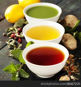 Tea concept. Different kinds of tea (black, green and matcha tea) in ceramic bowls and ingredients on wooden background