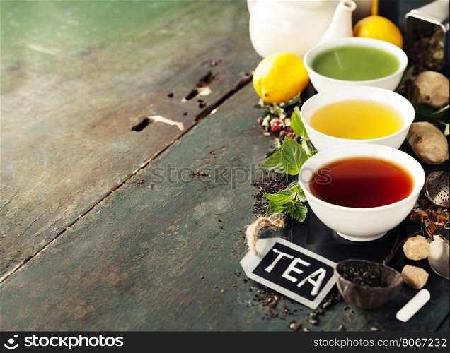 Tea concept. Different kinds of tea (black, green and matcha tea) in ceramic bowls and ingredients on wooden background