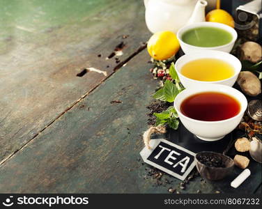 Tea concept. Different kinds of tea (black, green and matcha tea) in ceramic bowls and ingredients on wooden background