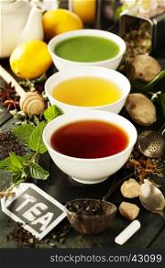 Tea concept. Different kinds of tea in ceramic bowls and ingredients on wooden background