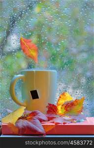 Tea cup at the window with leaves and drops after rain in autumn