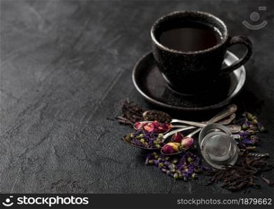 Tea cup with spoons and various tea on black. Black and green loose tea,rose buds,blue mallow flowers