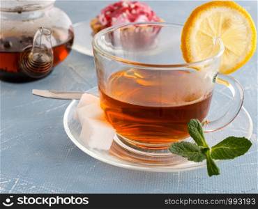 Tea cup with tea and mint leaves. Cakes and teapot in the background. Tea cup with tea and mint leaves.