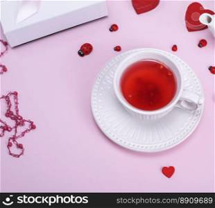 tea from berries of a viburnum in a white ceramic mug with a saucer on a pink background, top view