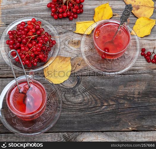 tea from fresh berries of viburnum in a transparent glass cup, fresh red berries on a gray wooden table, top view,