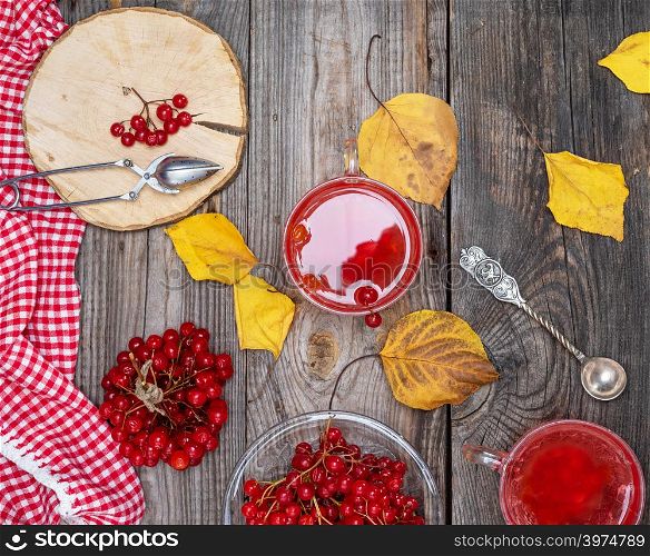 tea from fresh berries of viburnum in a transparent glass cup, fresh red berries on a gray wooden table, top view