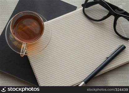 Tea, glasses and pens placed on a notebook for work