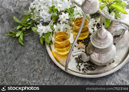 Tea glasses and pot, traditional sweets. Table setting with spring flowers