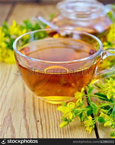 Tea in a glass cup and teapot, fresh flowers tutsan on the wooden board