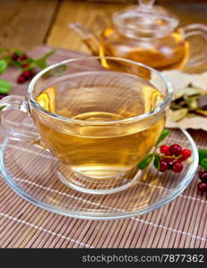 Tea in a glass cup, berries and green leaves lingonberry on a bamboo napkin on wooden boards background