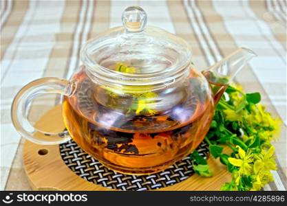 Tea in a glass teapot on stand, fresh flowers tutsan on the linen tablecloth background