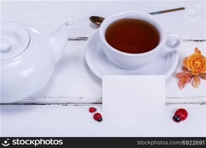 tea in a round white cup with a saucer on a white wooden background and an empty paper tag