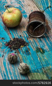 tea leaves and red apple on wooden background.The image is tinted in vintage style. tea leaves and red apple on wooden background