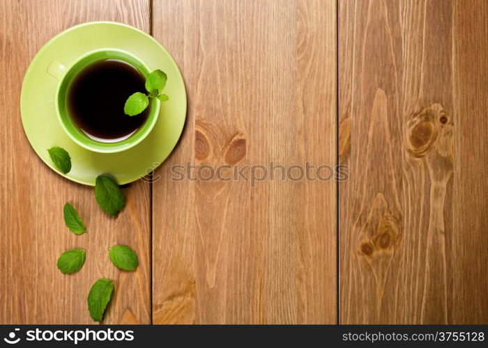 Tea mint in green cup with mint leaves on wooden table background. Top view