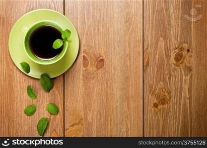 Tea mint in green cup with mint leaves on wooden table background. Top view