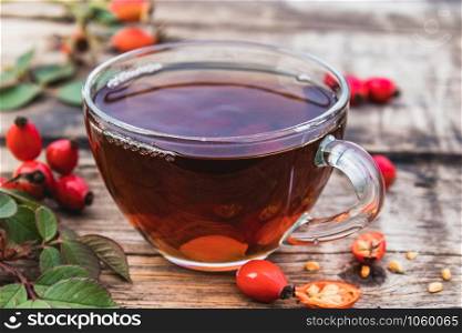 Tea or tincture with rose hips in a glass cup near red berries on a wooden table. Phytotherapy.. Tea or tincture with rose hips in a glass cup near red berries on a wooden table.