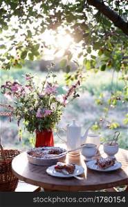tea party in the garden. on the table is a vase of flowers, pie with cherry and cup of tea 