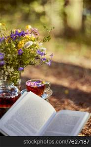 Tea party in the open air. Close-up of a Cup and teapot in nature in the forest. A bouquet of flowers and a book