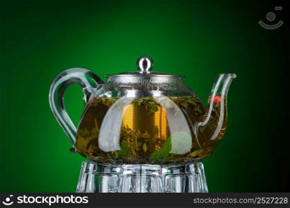 Tea with mint and herbs in a transparent teapot on a green background. Isolated with backlight. Mint tea in a transparent teapot