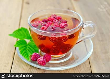 Tea with raspberries in a glass cup, green raspberry leaf on the background of wooden boards