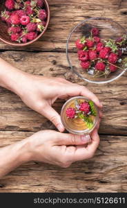 Tea with raspberries. Tea cup with raspberry warming tea in hands on vintage wooden background